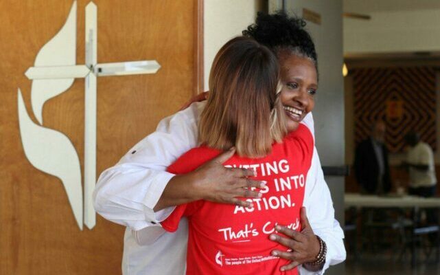 Two people hugging next to a United Methodist logo