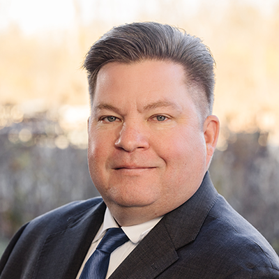 Andy Sorka wearing a suit and tie and smilling.