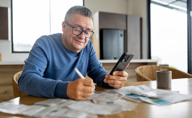 Happy man paying bills online using his cell phone