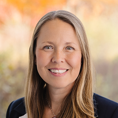 Portrait of Kelly Wittich smiling. She has long blonde hair and is wearing a black blazer.