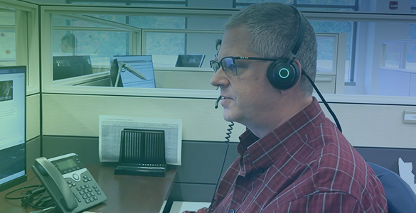 A man is seated at a desk wearing a headset with a microphone.