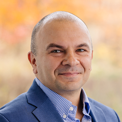 Portrait of Piotr Chwala smiling. He's wearing a blue blazer and a light blue collared shirt.