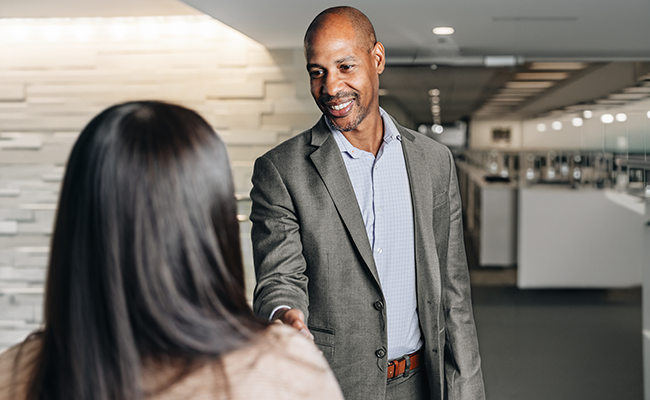 A man wearing a suit extending his arm to shake a woman's hand.