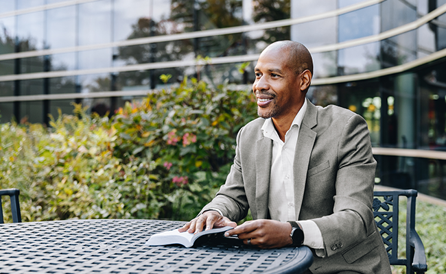 A male business professional sitting outside smiling.