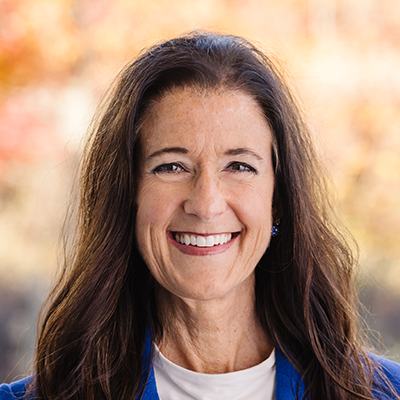 Portrait of Rev. Rachel Miller smiling. She has long brown hair and is wearing a blue blazer and white blouse.